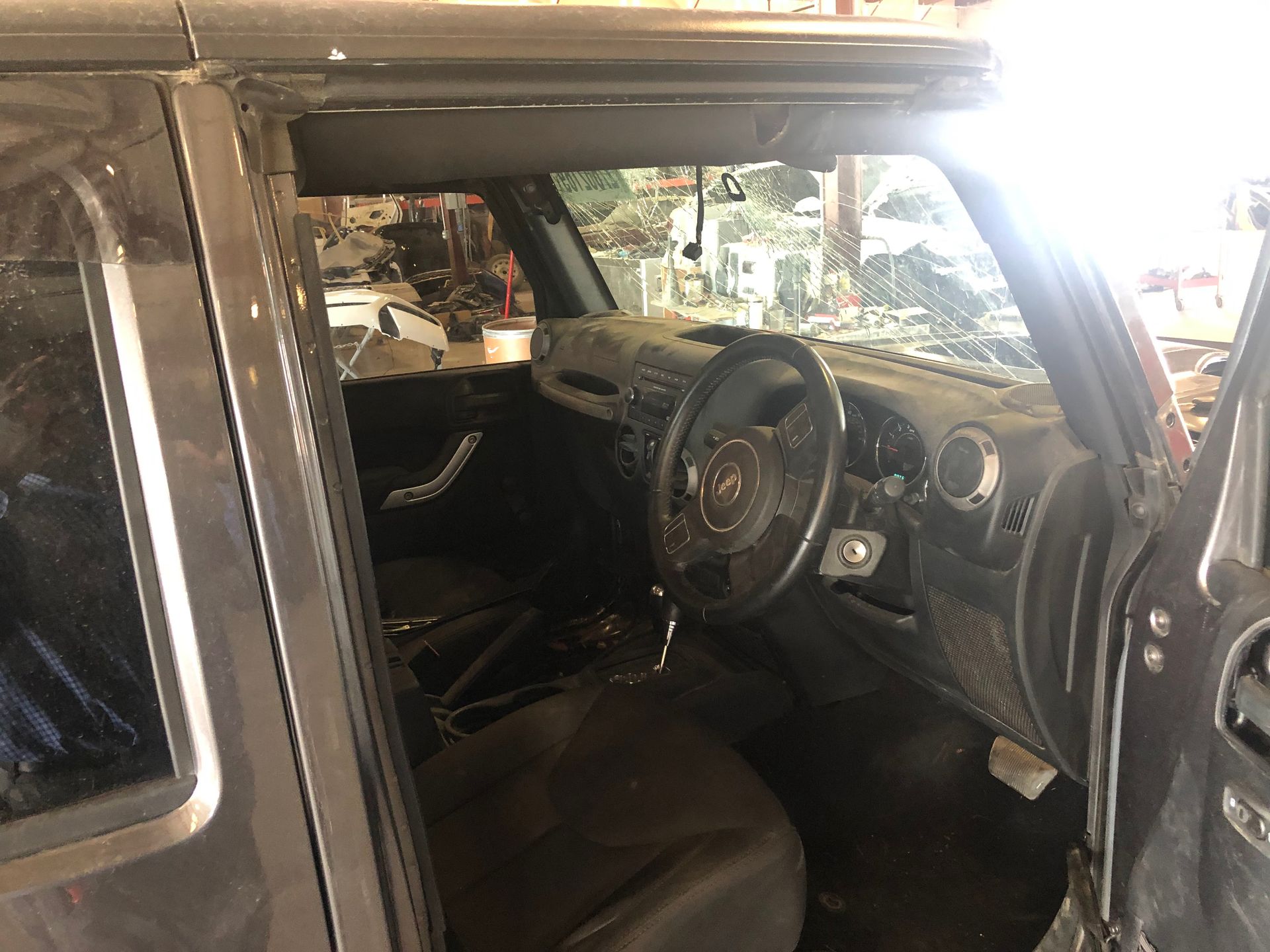 Interior view of a black Jeep Wrangler with the driver's side door open. Dashboard, steering wheel, and seats are visible.