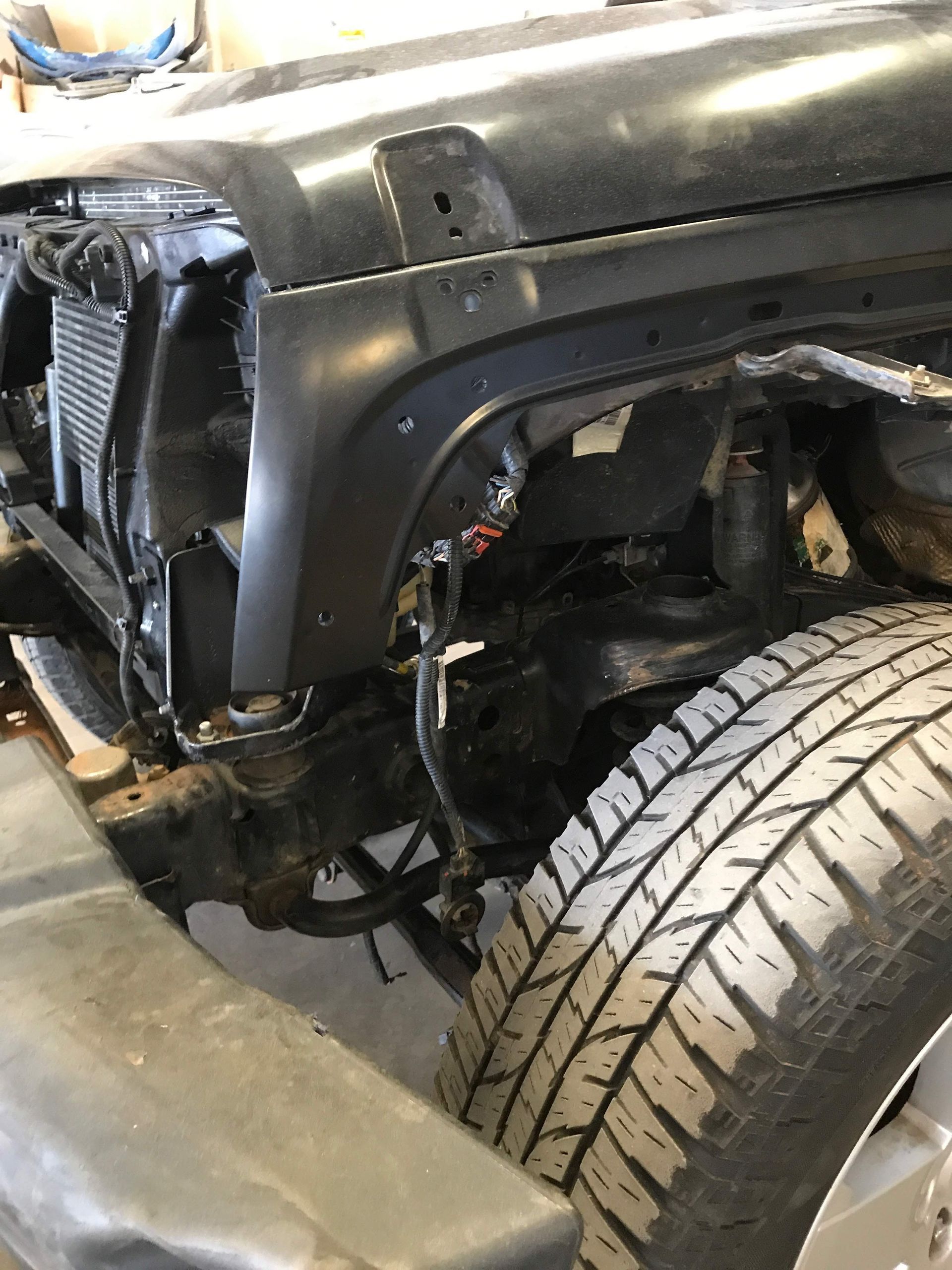 Black Jeep Wrangler front end with a tire and fender, partially disassembled, in a shop setting.