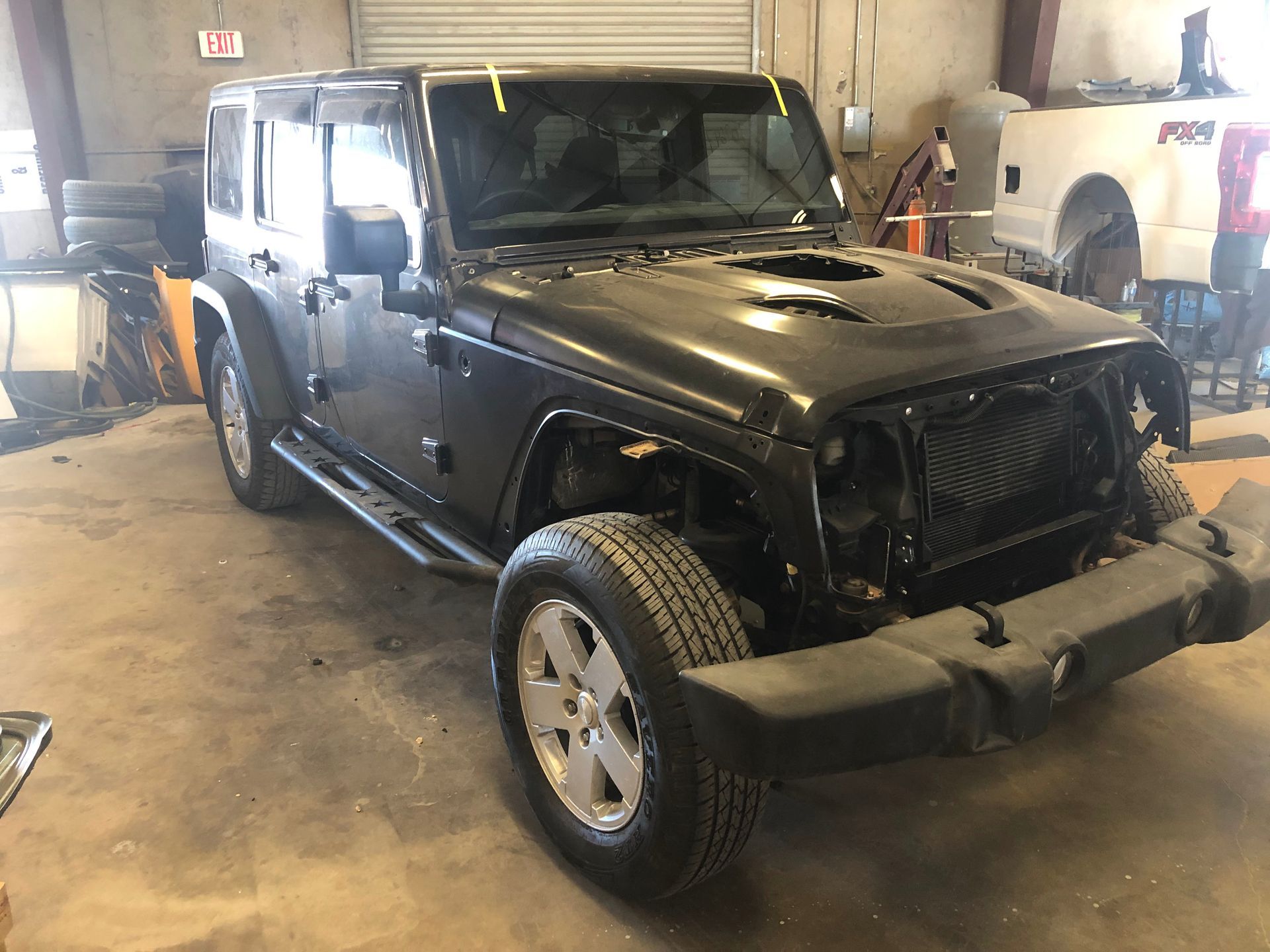 Black Jeep Wrangler in a garage, front grill and bumper removed.