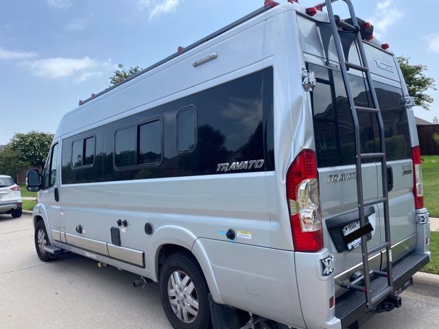Silver RV with black windows and ladder, parked outdoors.