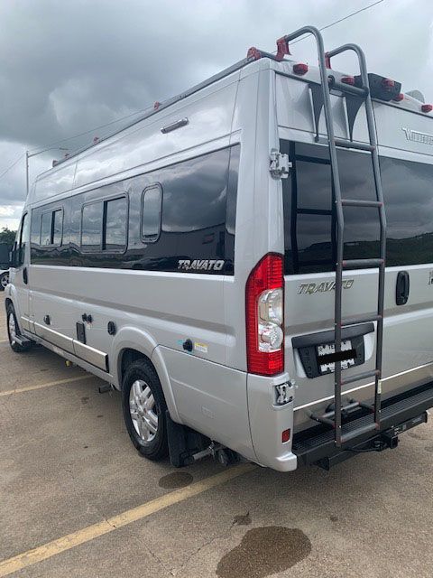 Silver RV with ladder, parked on pavement, under a cloudy sky.