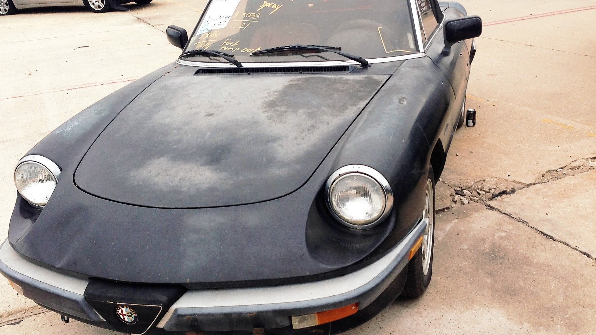 Dark blue Alfa Romeo Spider convertible, weathered exterior, parked outdoors.
