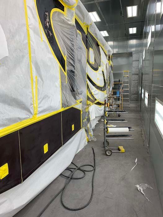 Side view of a vehicle being painted in an auto body shop, masked in plastic and tape.