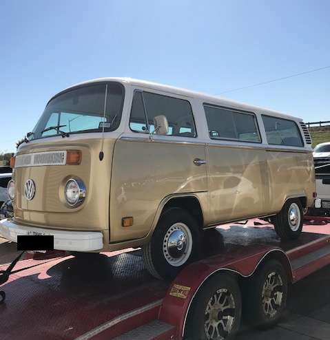 Gold and white Volkswagen bus on a red trailer, parked outside on a sunny day.