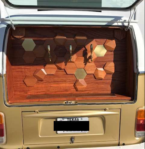 Rear of gold and white VW van with a custom wooden bar, honeycomb design, and two beer taps.