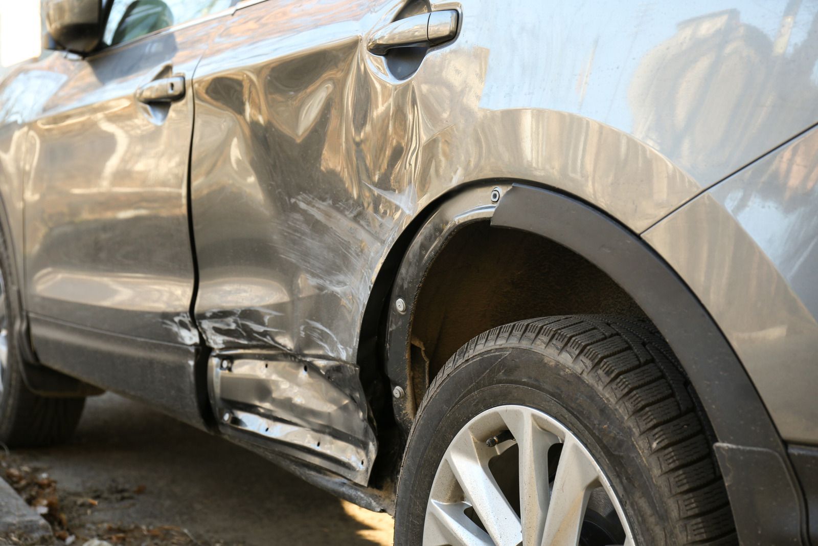 Damaged gray car door and rear quarter panel, showing significant dents and scratches after a collision.