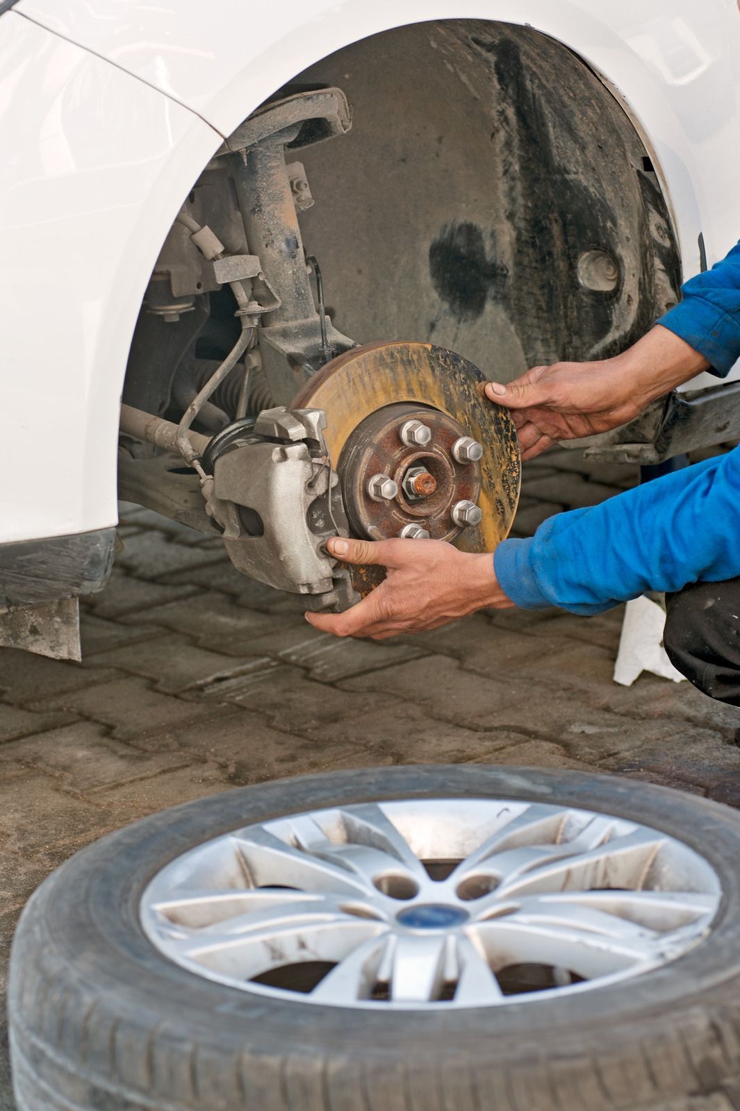Mechanic replacing a brake rotor on a car. Rusty rotor, silver rim, and a tire on the ground.