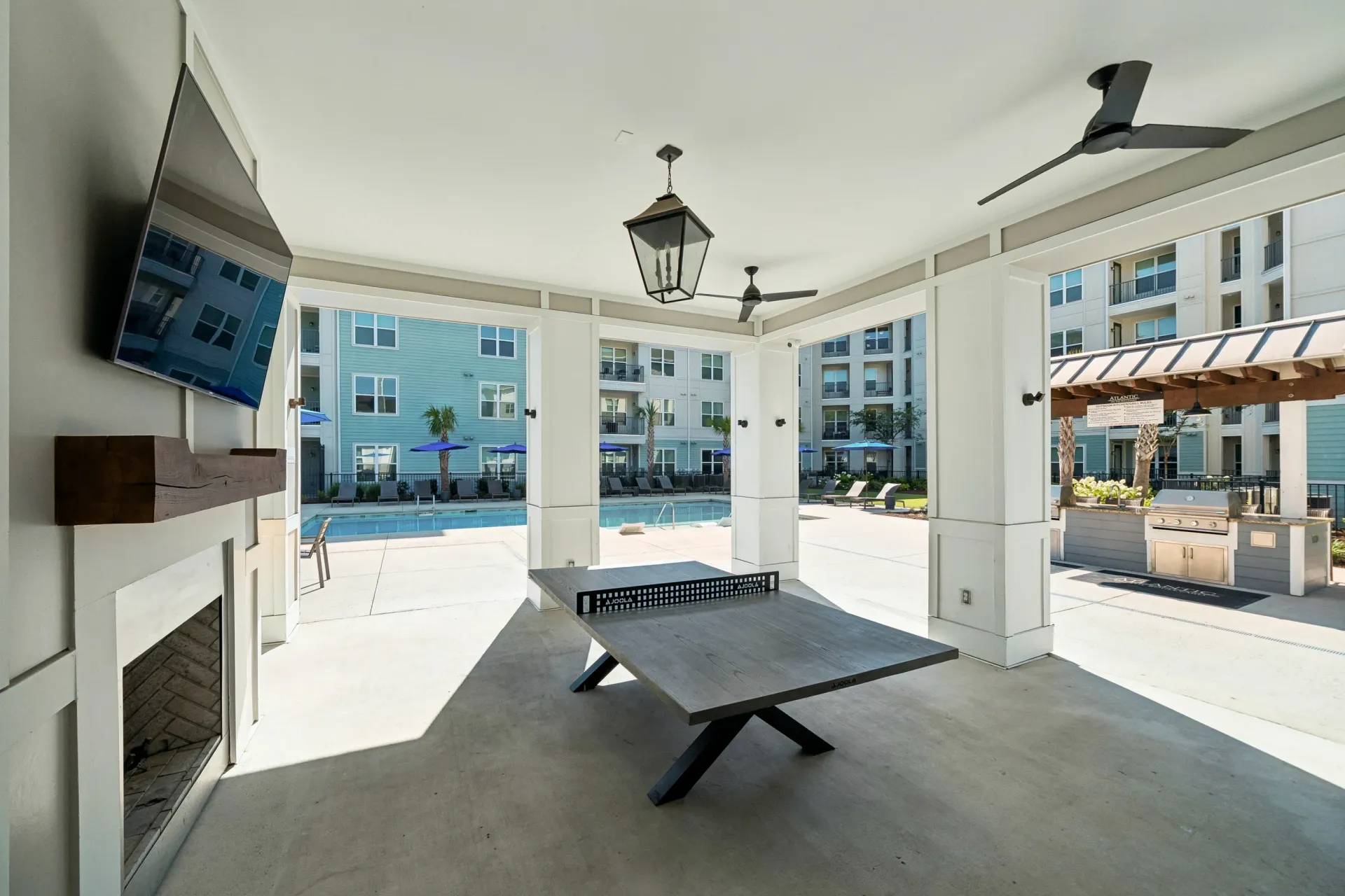Covered outdoor lounge with ping pong table, fireplace, and TV overlooking pool and apartment buildings at Atlantic on the Boulevard in North Charleston, SC.