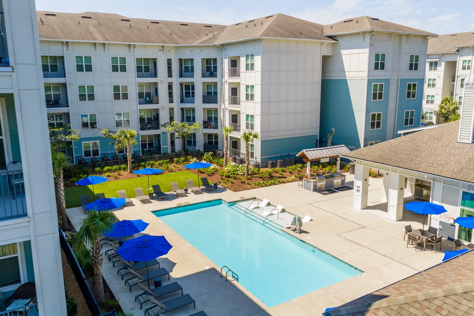 Outdoor swimming pool with lounge chairs and umbrellas next to apartment buildings at Atlantic on the Boulevard in North Charleston, SC.