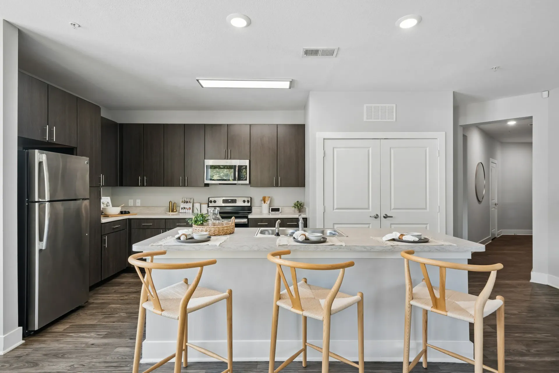 Modern kitchen with dark wood cabinets, stainless steel appliances, and a large island with bar stools.
