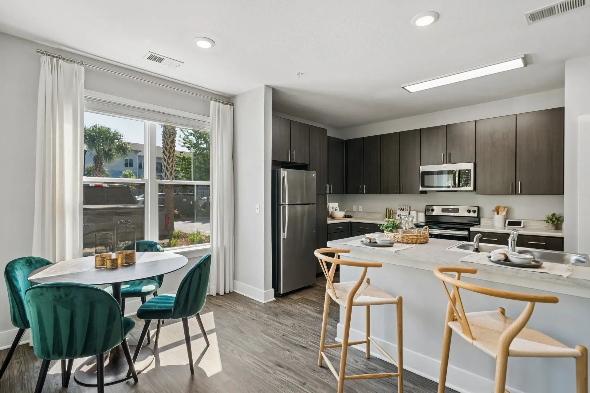 Modern kitchen and dining area with dark wood cabinets, stainless steel appliances, and a dining table with green velvet chairs at Atlantic on the Boulevard in North Charleston, SC.