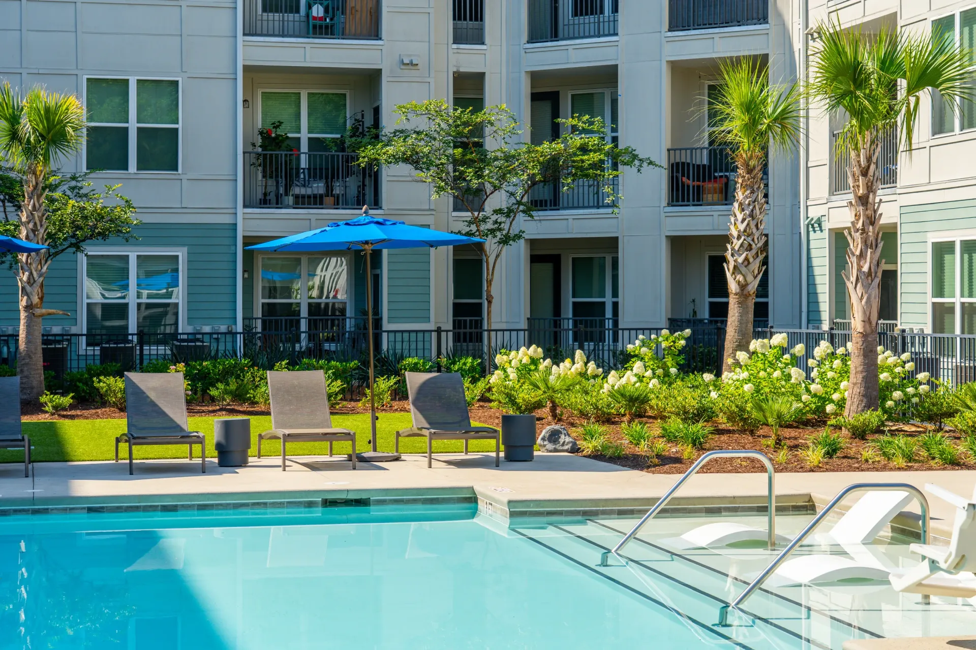 Resort-style swimming pool with lounge chairs and umbrellas in front of apartment buildings at Atlantic on the Boulevard in North Charleston, SC.