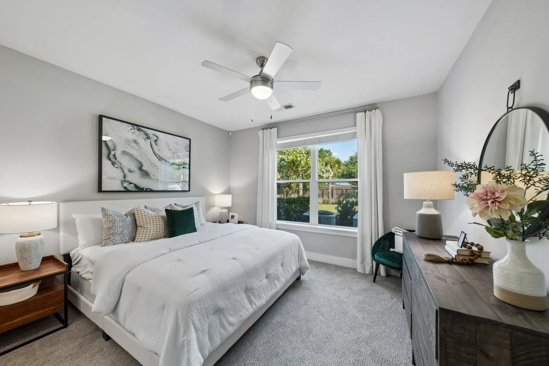 Stylish bedroom with a king-size bed, ceiling fan, and large window overlooking a green backyard at Atlantic on the Boulevard in North Charleston, SC.