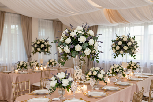 Elegant wedding reception with white and blush floral centerpieces and gold chairs under draped white ceilings