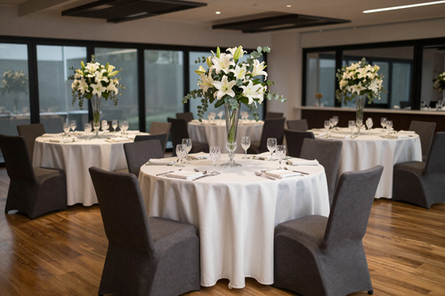Round banquet tables with white linens and tall white floral centerpieces in a modern event room