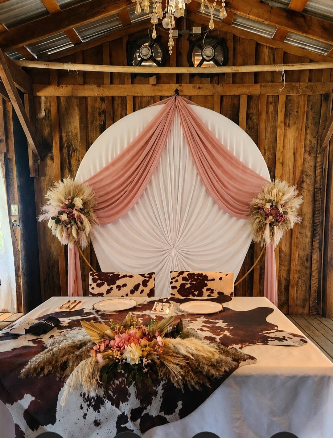 Rustic wedding backdrop with blush draping, round white panel, and floral arrangement on a table