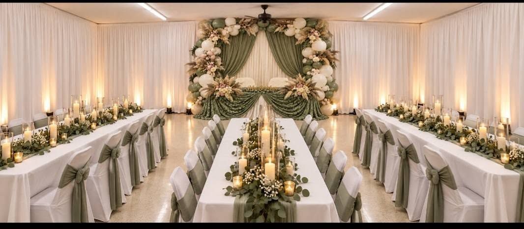 Elegant wedding reception with long white tables, floral centerpieces, and a greenery arch at the head table