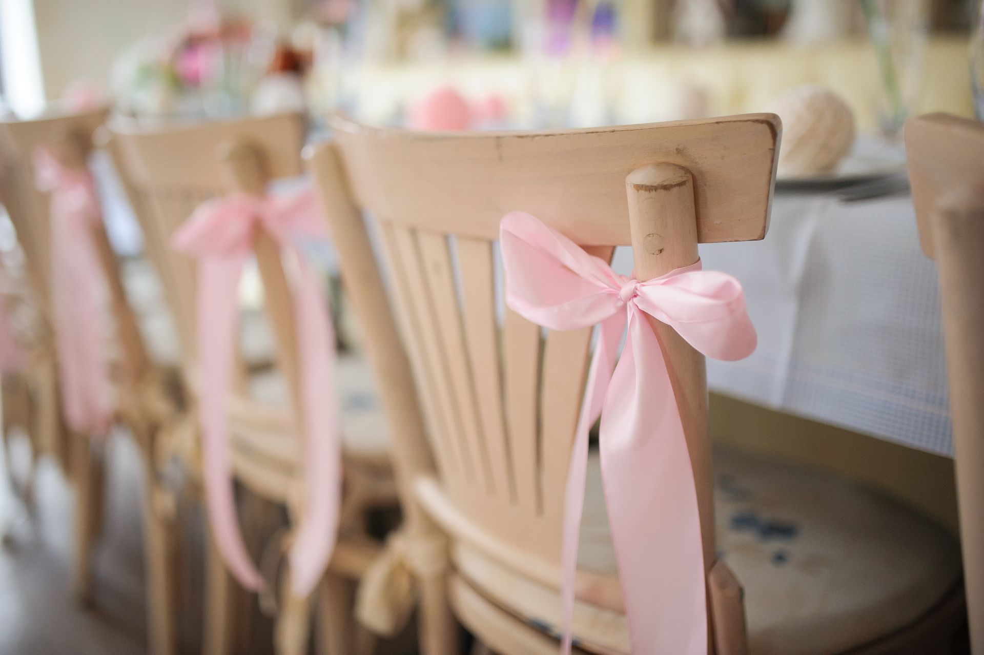 Pink ribbon bows tied to wooden dining chairs at a decorated table setup