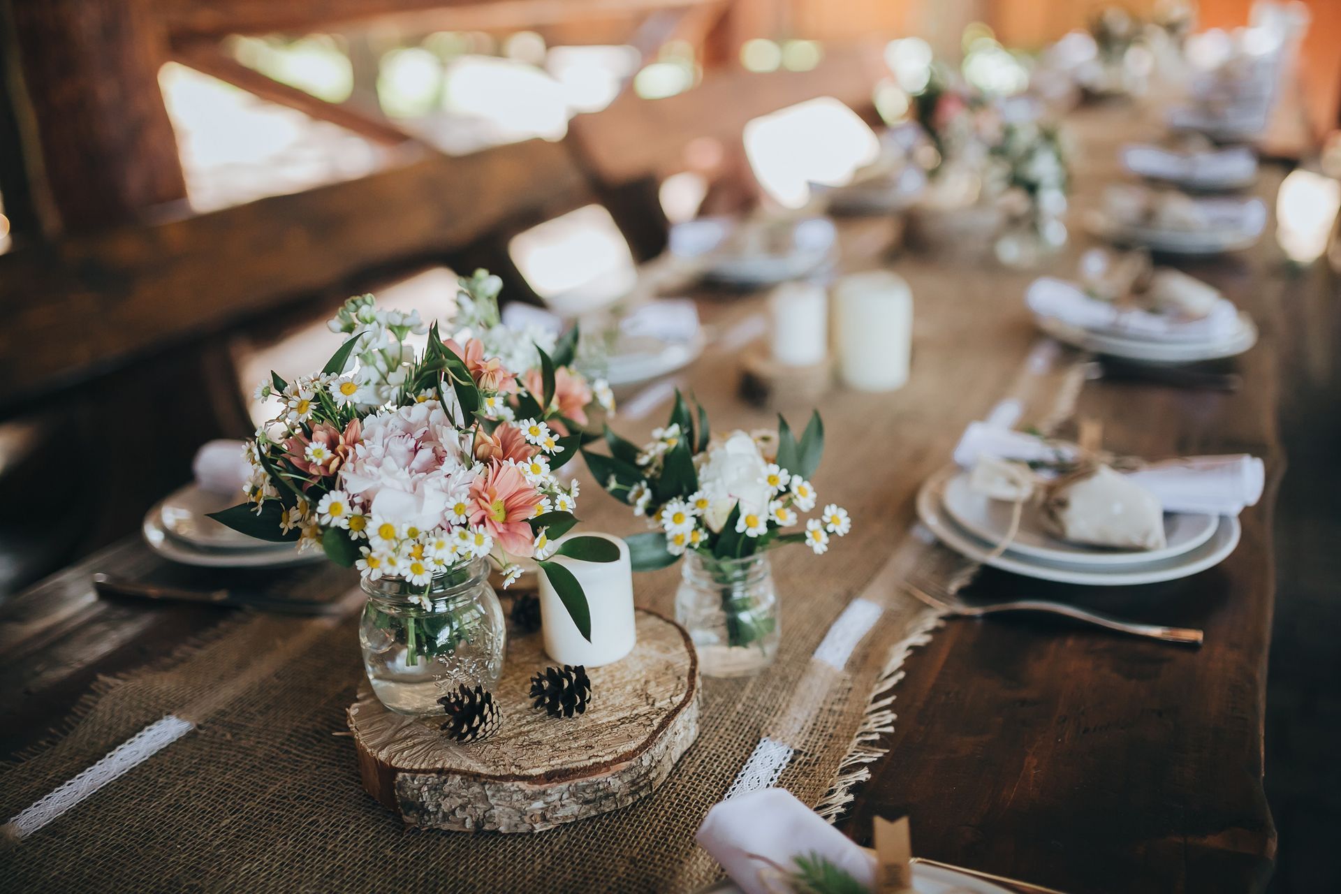 Rustic wedding reception table with floral centerpieces, candles, and white place settings