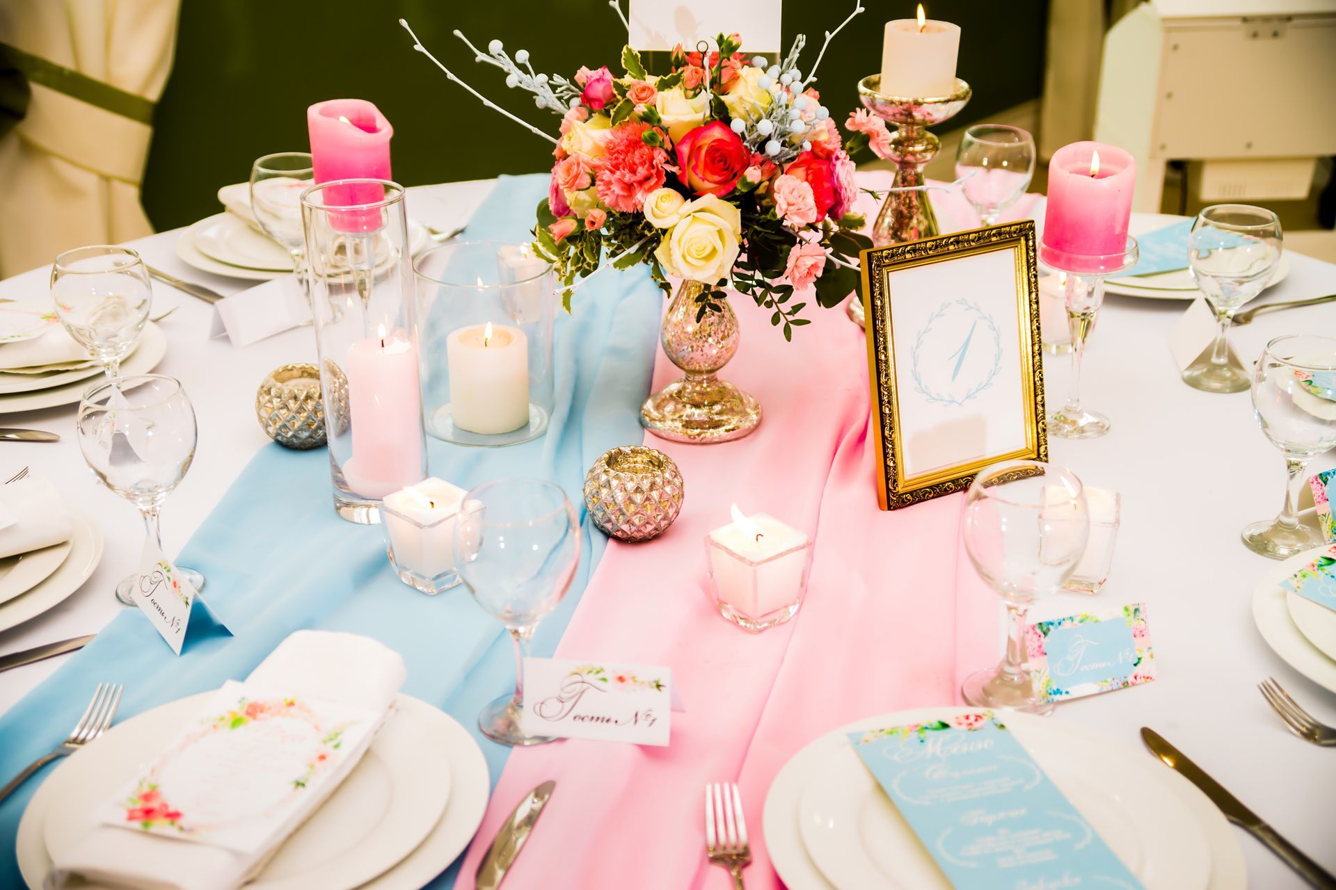 Elegant pink-and-gold table setting with flowers, candles, and place cards for a formal event