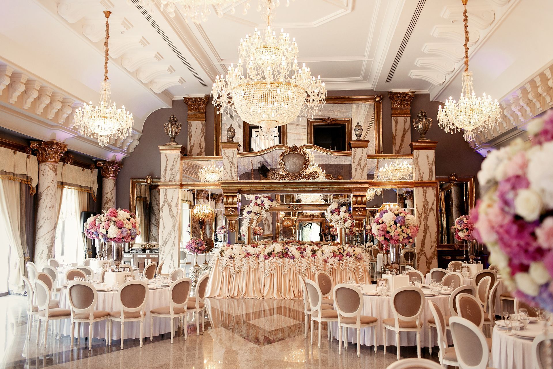 Elegant banquet hall with chandeliers, white chairs, and floral decor set for a formal event