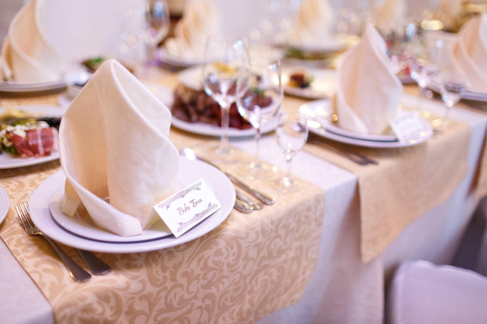 Elegant banquet table set with folded cream napkins, white plates, and floral tablecloths at a reception