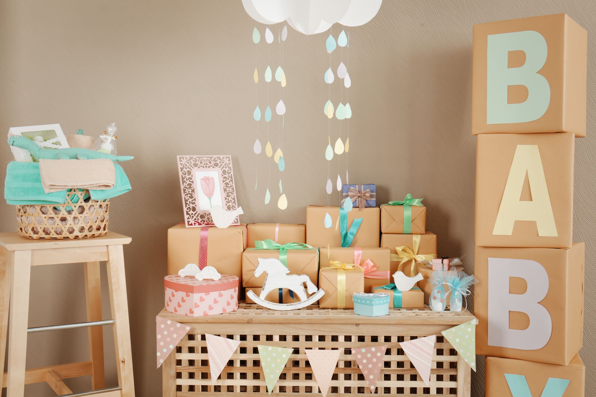 Baby shower dessert table with pastel gifts, cupcakes, and large “BABY” blocks in a tan room