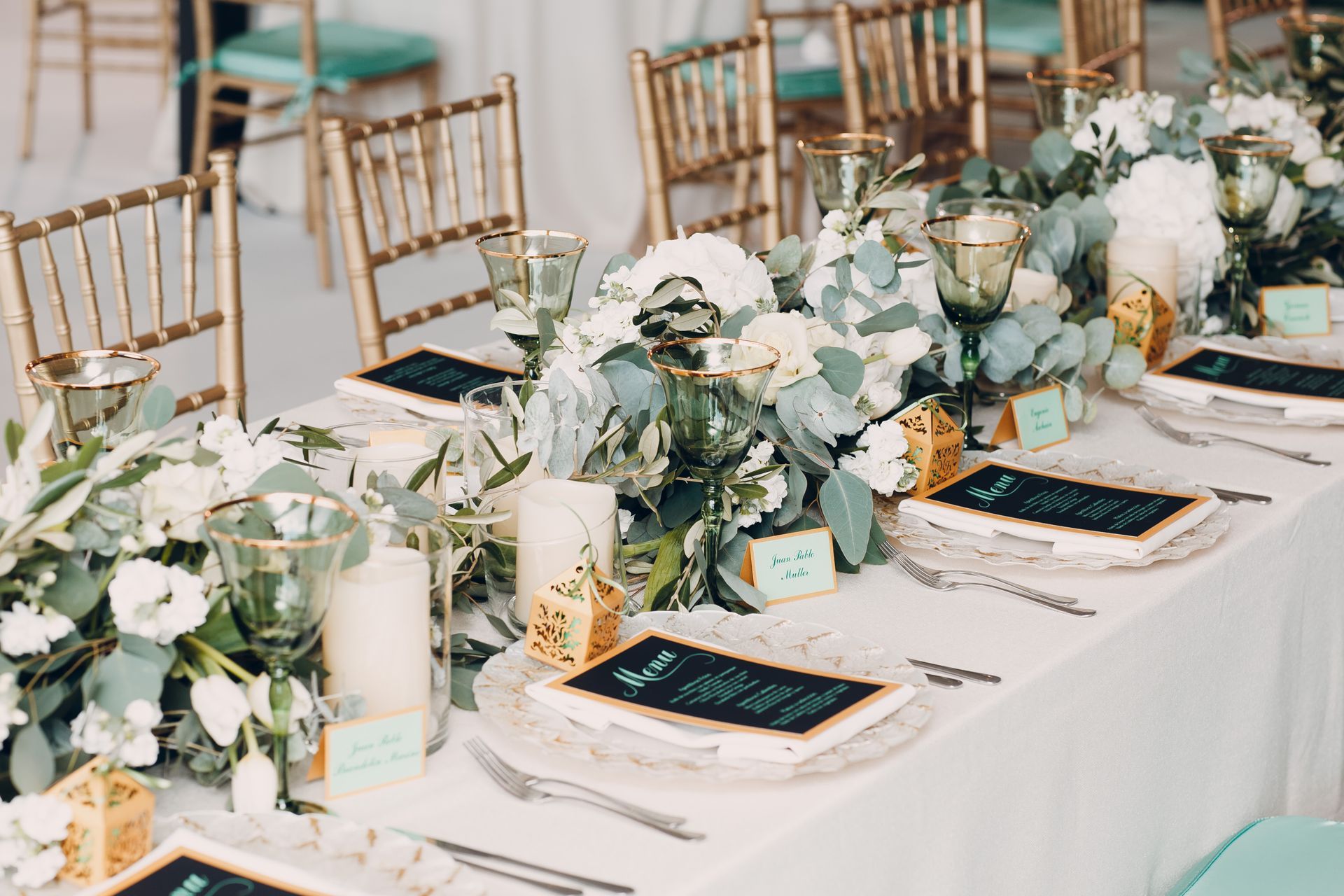 Elegant wedding reception table with white florals, greenery, candles, and gold chairs