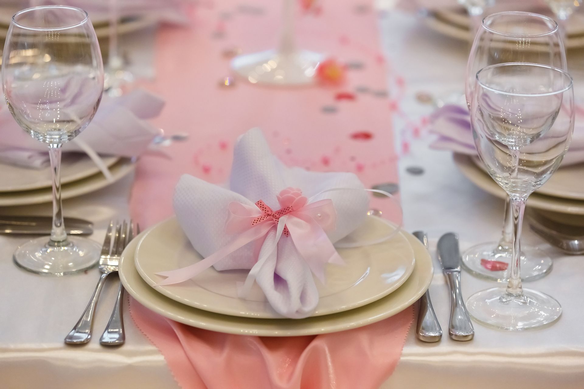 Elegant banquet table with pink runner, folded napkins, glassware, and silverware set for an event