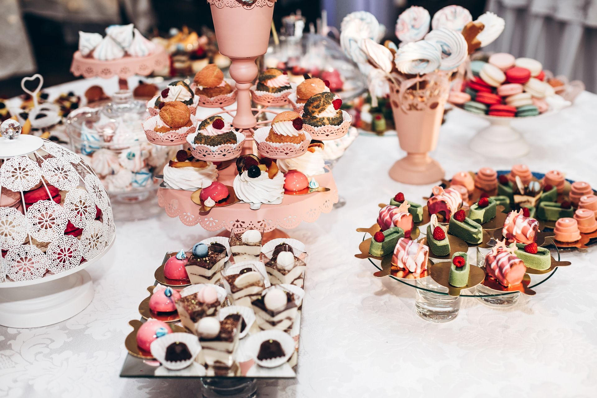 Assorted colorful mini desserts and pastries arranged on a buffet table with decorative stands