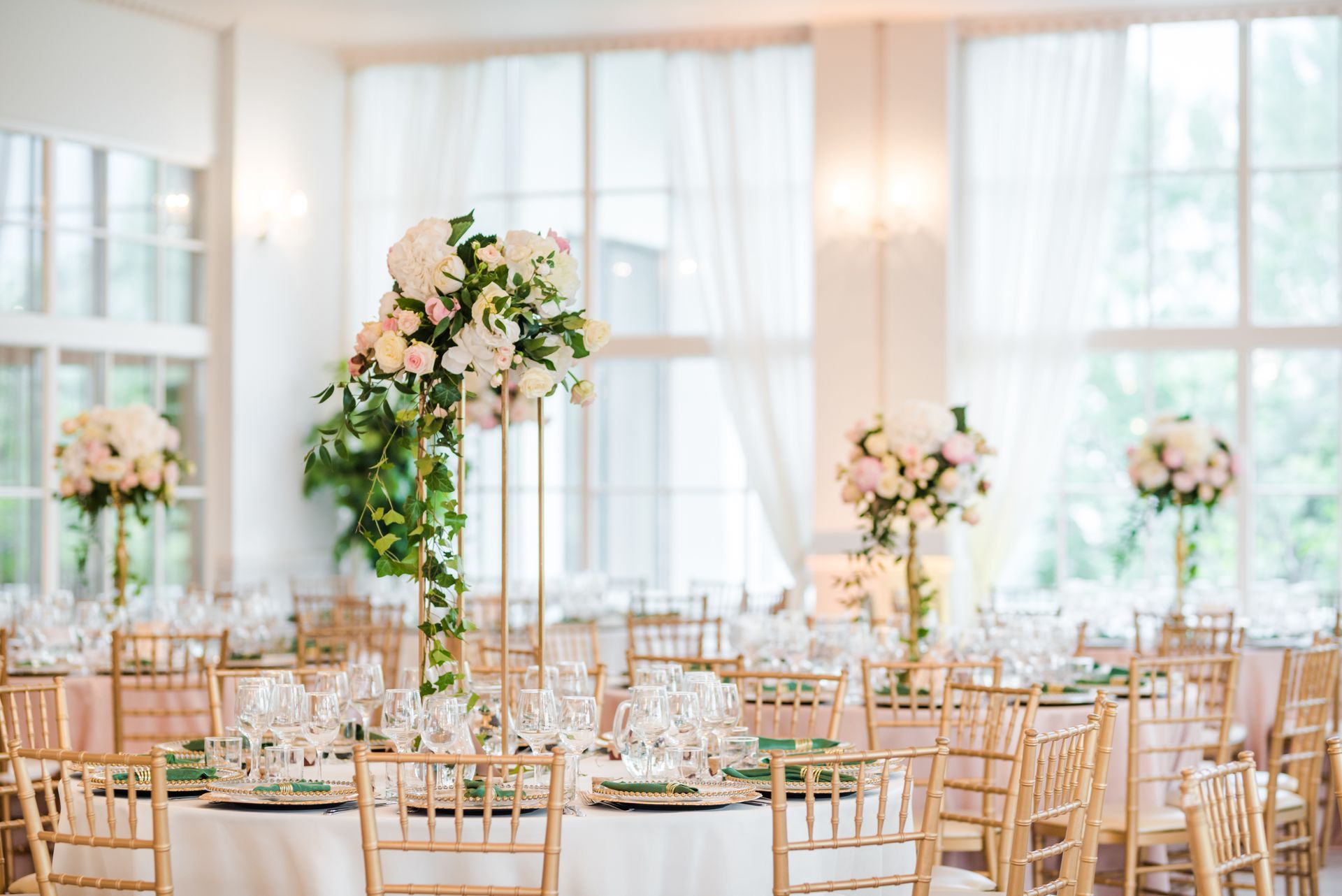 Elegant wedding reception with gold chairs, white floral centerpieces, and bright windowed banquet hall