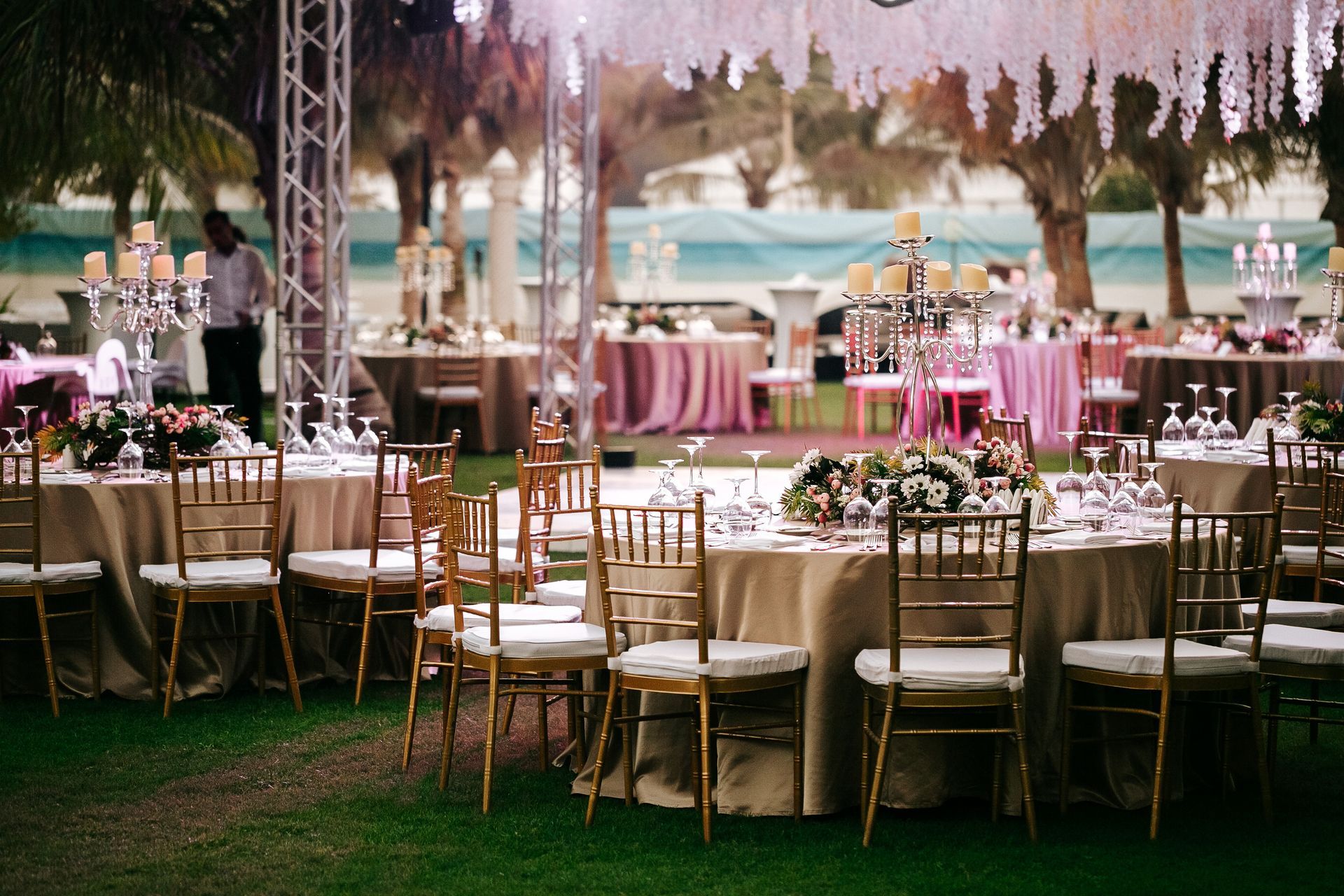 Elegant outdoor wedding reception with pink tablecloths, gold chairs, and hanging floral decorations under a tent