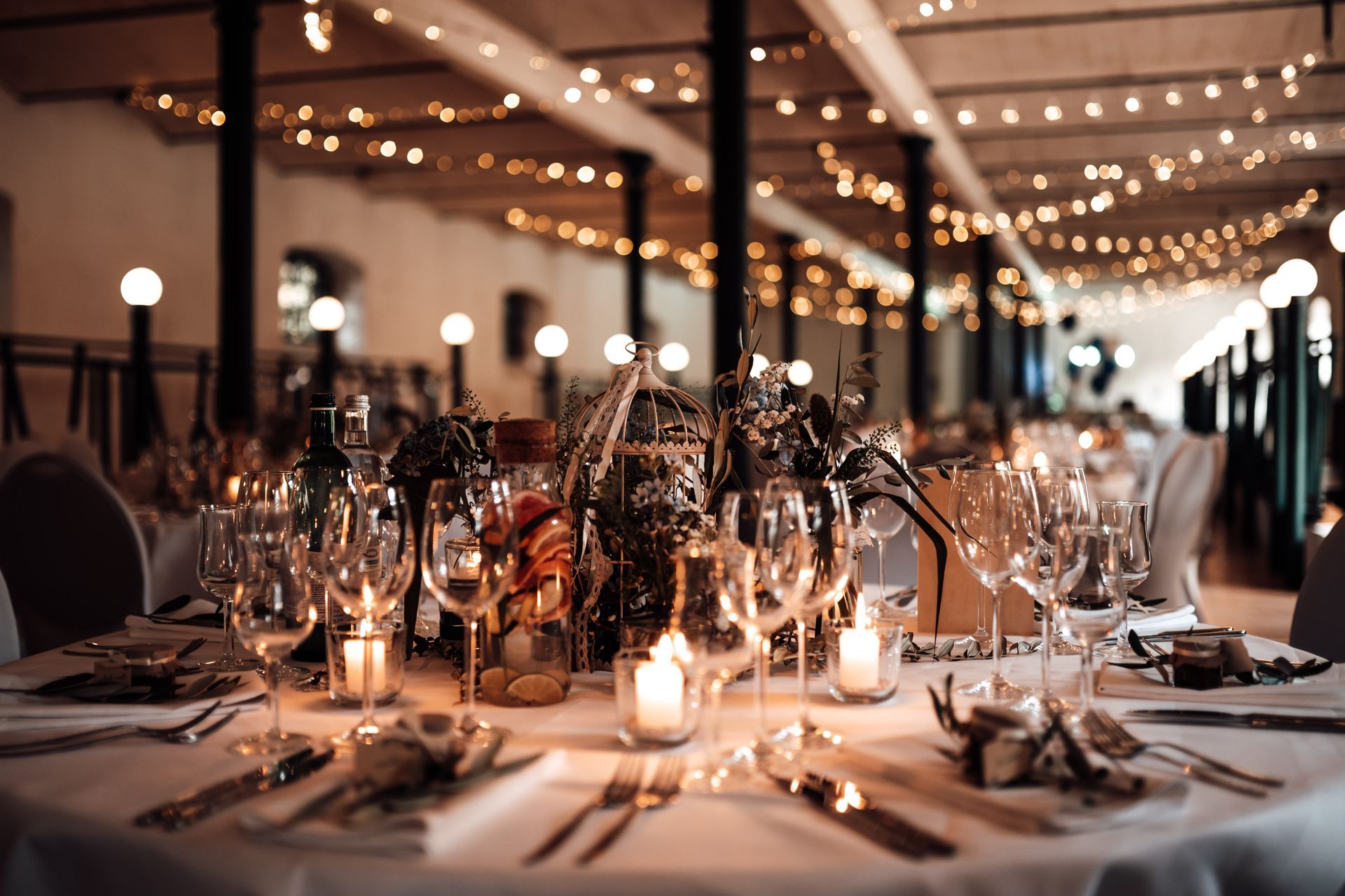 Elegant candlelit banquet table under string lights in a softly lit event hall