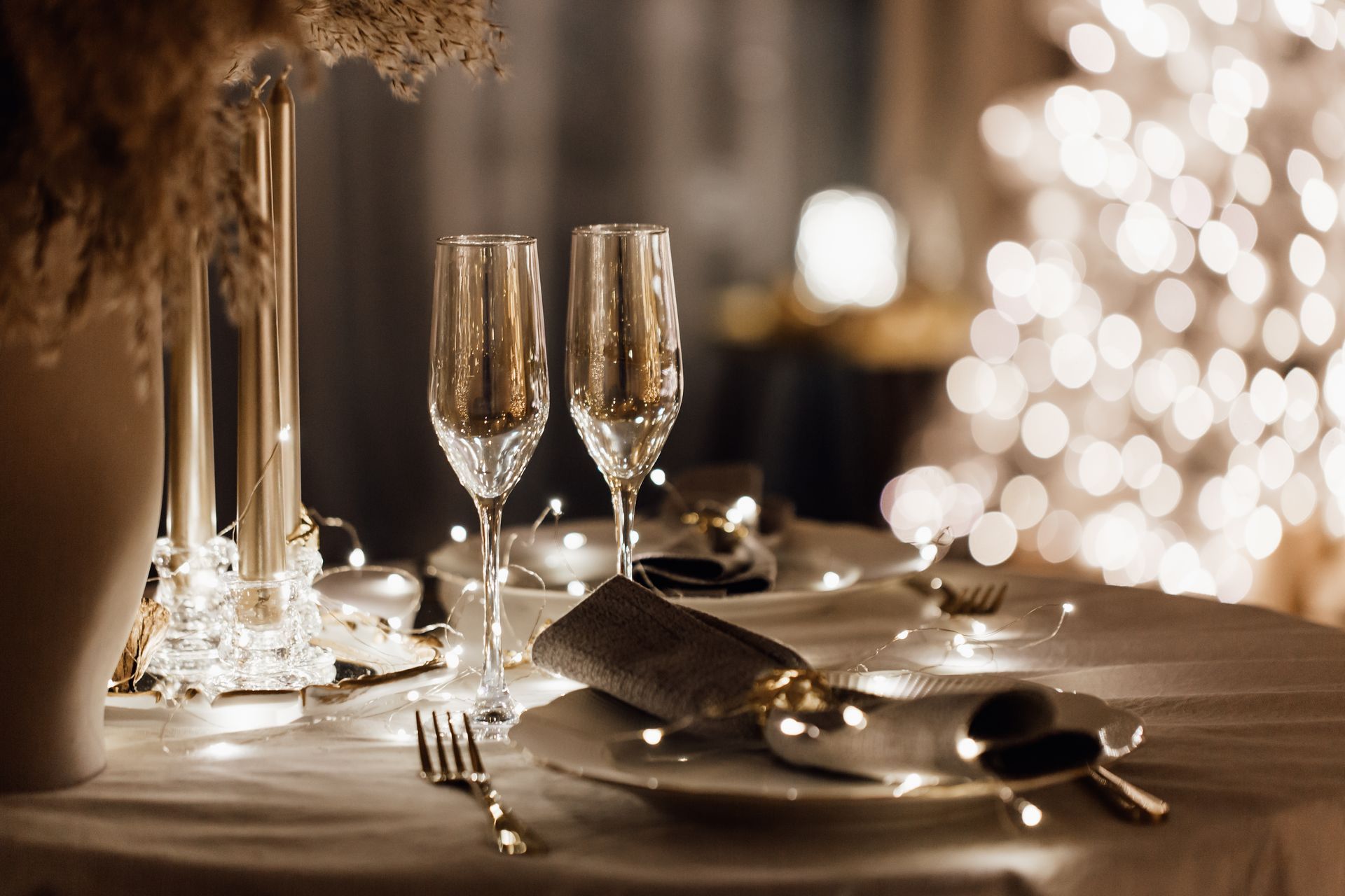 Elegant candlelit dinner table with champagne flutes, silverware, and warm glowing bokeh lights