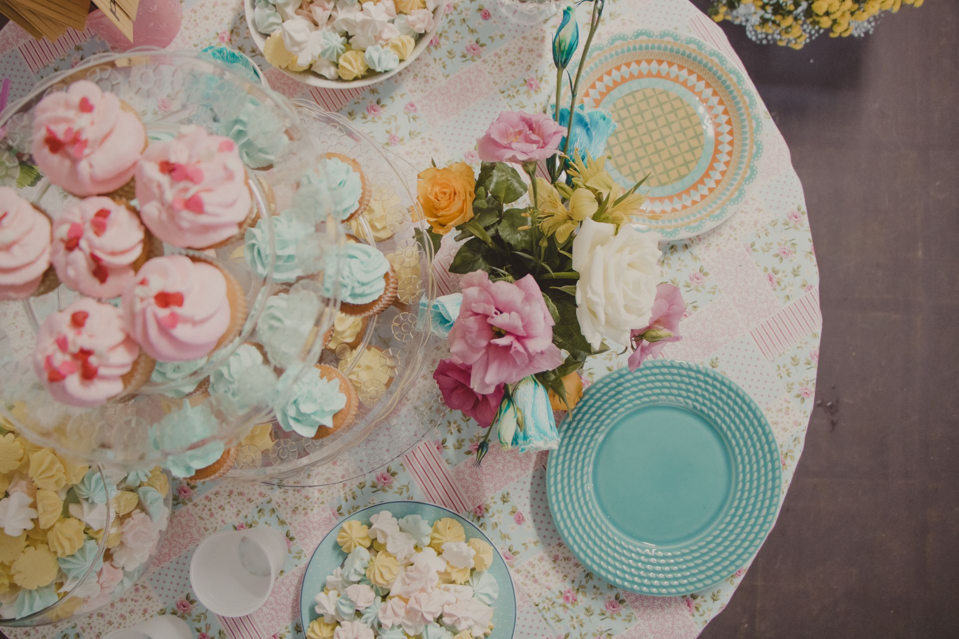 Pastel dessert table with cupcakes, macarons, flowers, and teal plates on a lace tablecloth