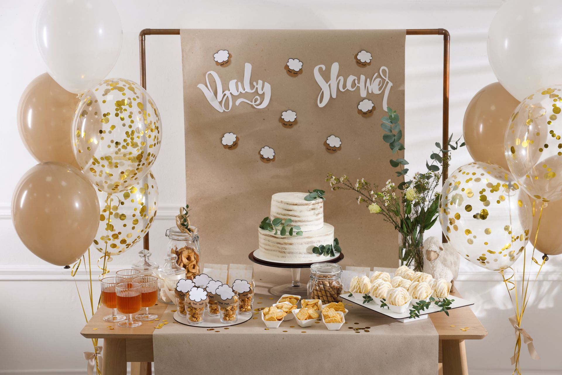 Baby shower dessert table with white and gold balloons, cupcakes, and a cake backdrop reading “Baby S…”