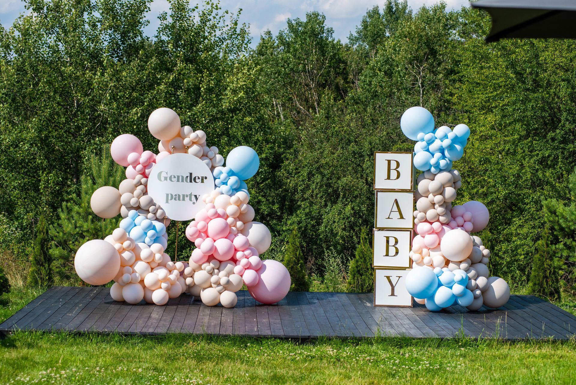 Baby shower balloon display with pastel pink and blue balloons and “BABY” blocks on a grassy lawn