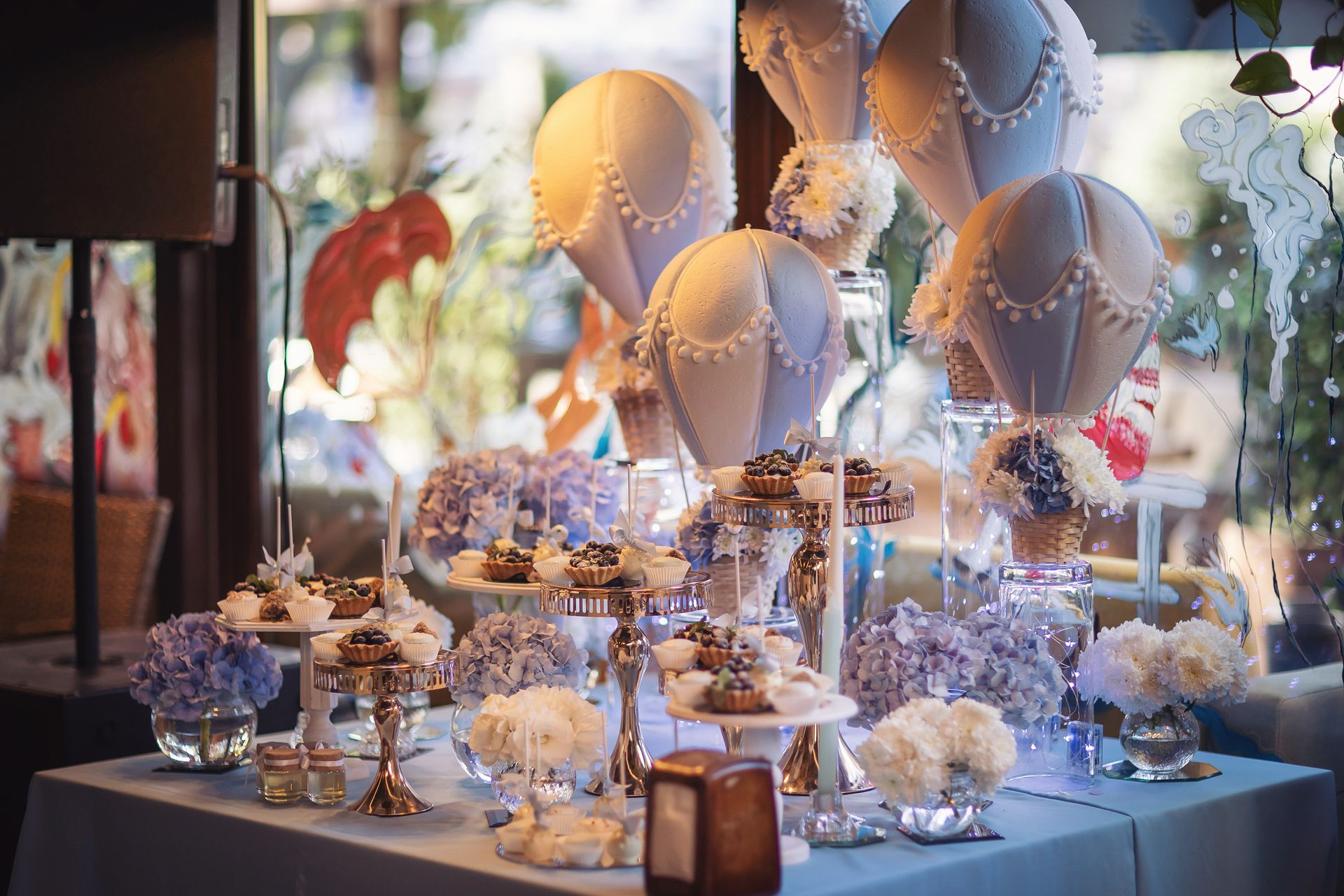 Elegant dessert table with pastel balloons, flowers, and cakes at a party event