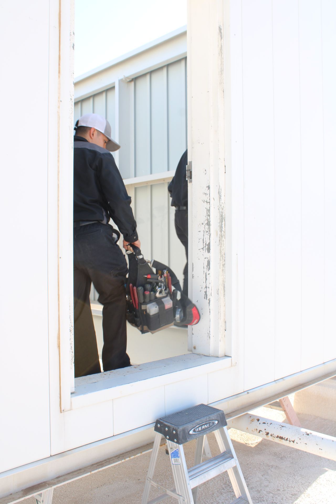 A man is carrying a tool bag while standing next to a ladder.