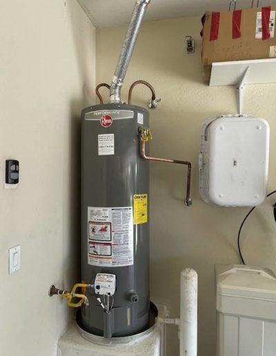 A gray water heater is sitting in a laundry room next to a washer and dryer.