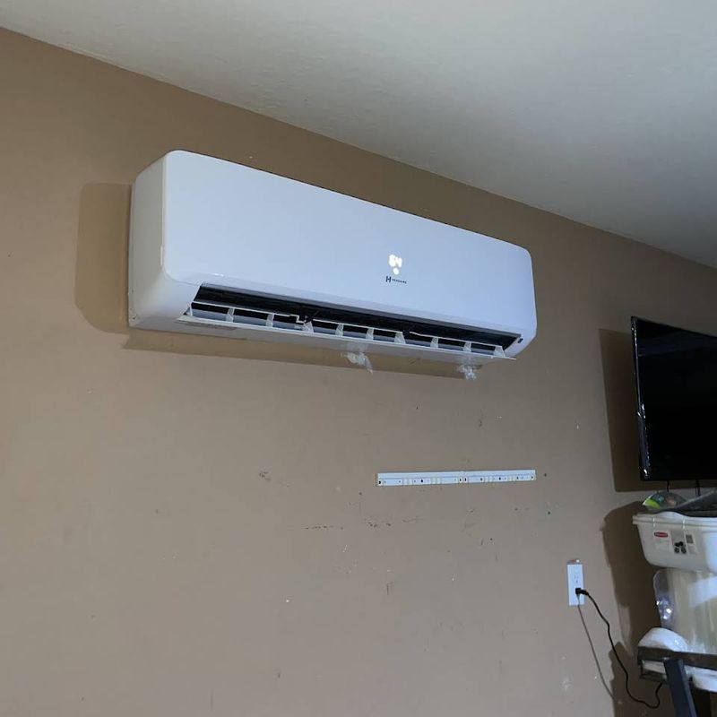 A white air conditioner is mounted on a wall next to a television.