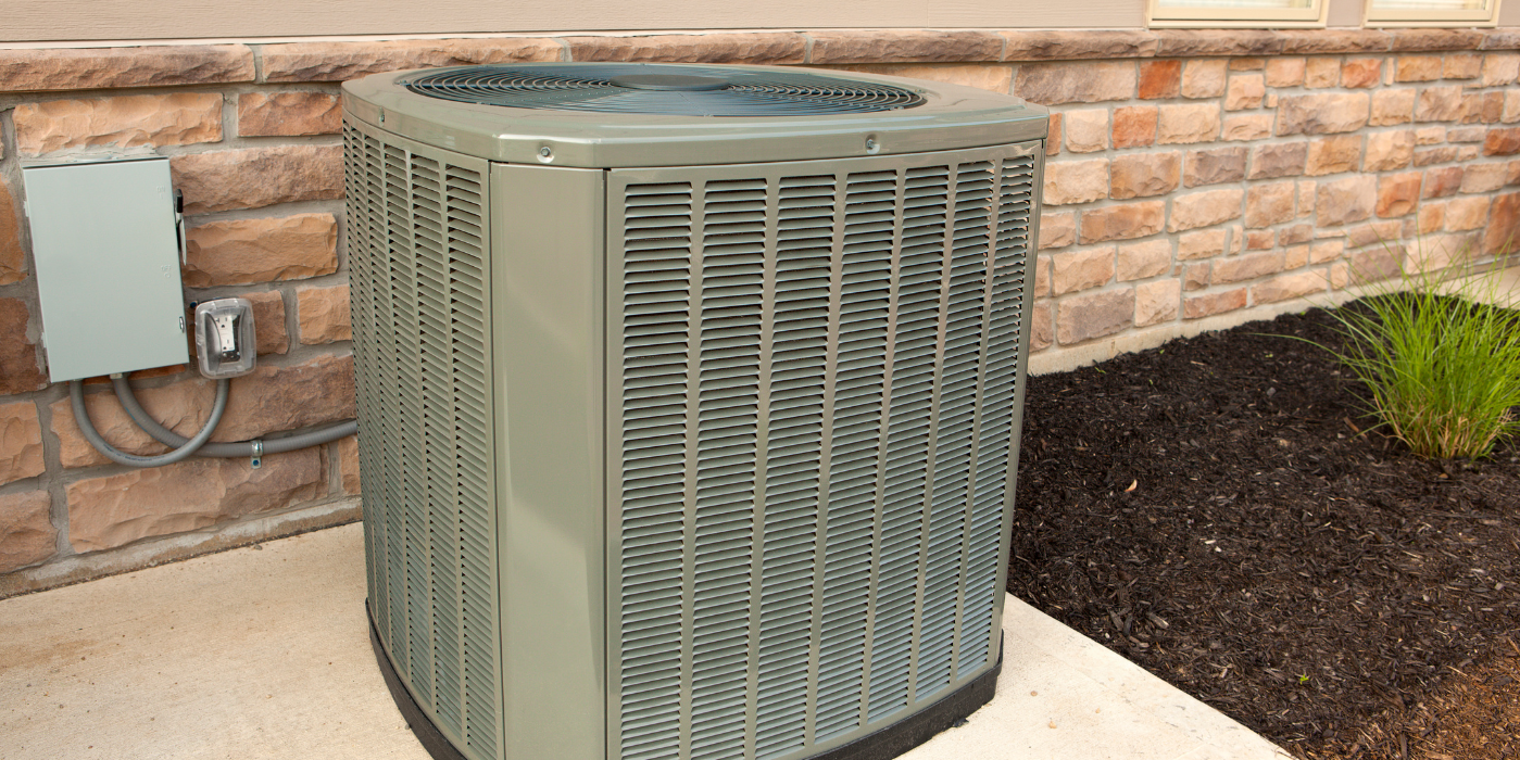 An air conditioner is sitting on a sidewalk next to a brick wall.
