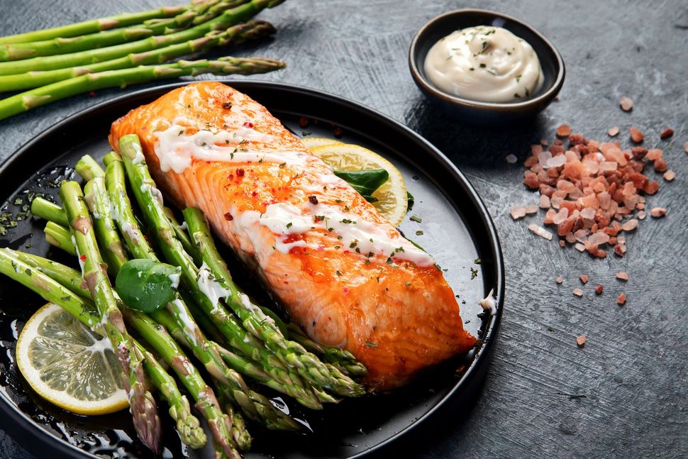A black plate topped with salmon and asparagus on a table.