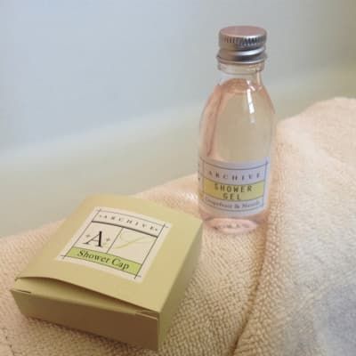 A shower cap and a bottle of shower gel are on a towel.