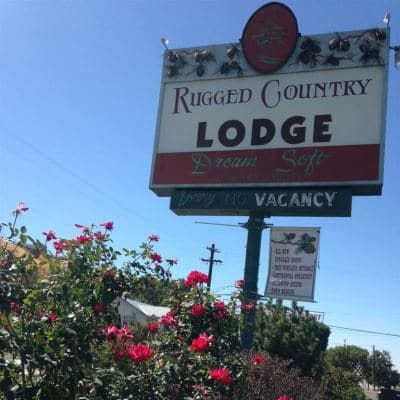 A sign for rugged country lodge is surrounded by flowers