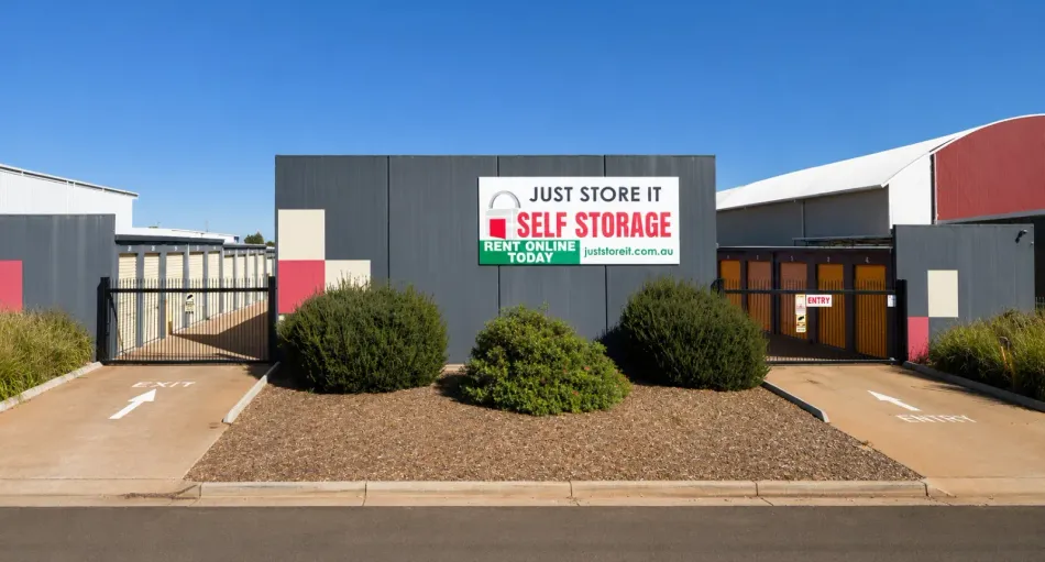 Just Store It self storage facility with gray buildings, red accents, and landscaped entrance under a clear sky
