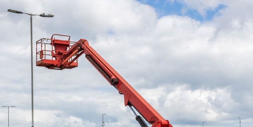 A red crane is lifting a street light in a parking lot.— BDM Heavy Vehicle Repairs In Wauchope, NSW