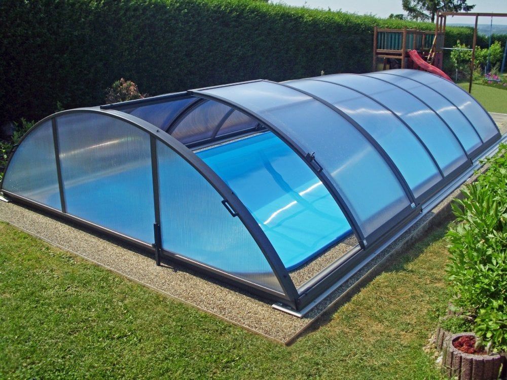 Niedrige, gewölbte blaue Poolabdeckung in einem grasbewachsenen Garten neben einer Hecke