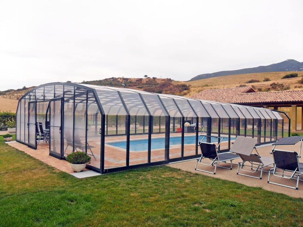 Innenpool in einem Glasgewächshaus neben einer Terrasse mit Liegestühlen, eingebettet in eine Wüstenlandschaft