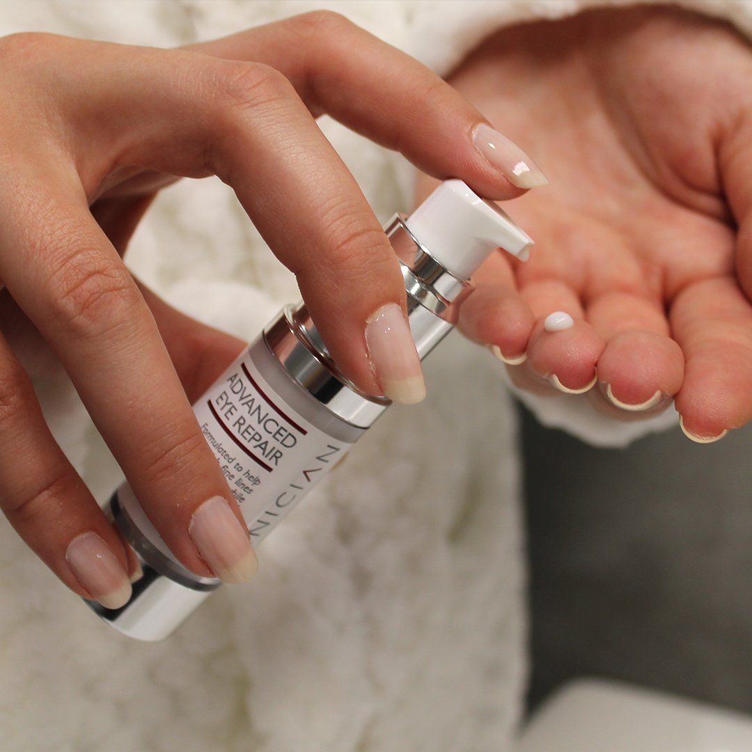 Woman dispensing eye cream from a silver bottle onto her palm.